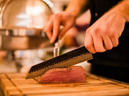 Restaurant Gronau: Seeblick Close-up of hands slicing red meat on a wooden cutting board