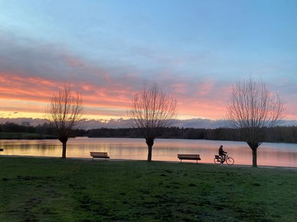 Hotel Seeblick in Gronau Fahrradfahrer am Seeufer bei Sonnenuntergang mit Bänken und kahlen Bäumen