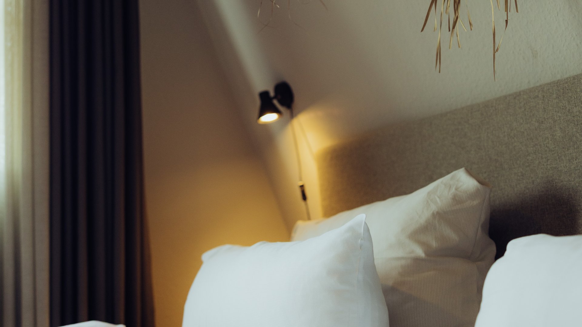 Seeblick: Ferienwohnungen Gronau Bett mit weißen Kissen, Wandlampe und getrockneter Palmendekoration