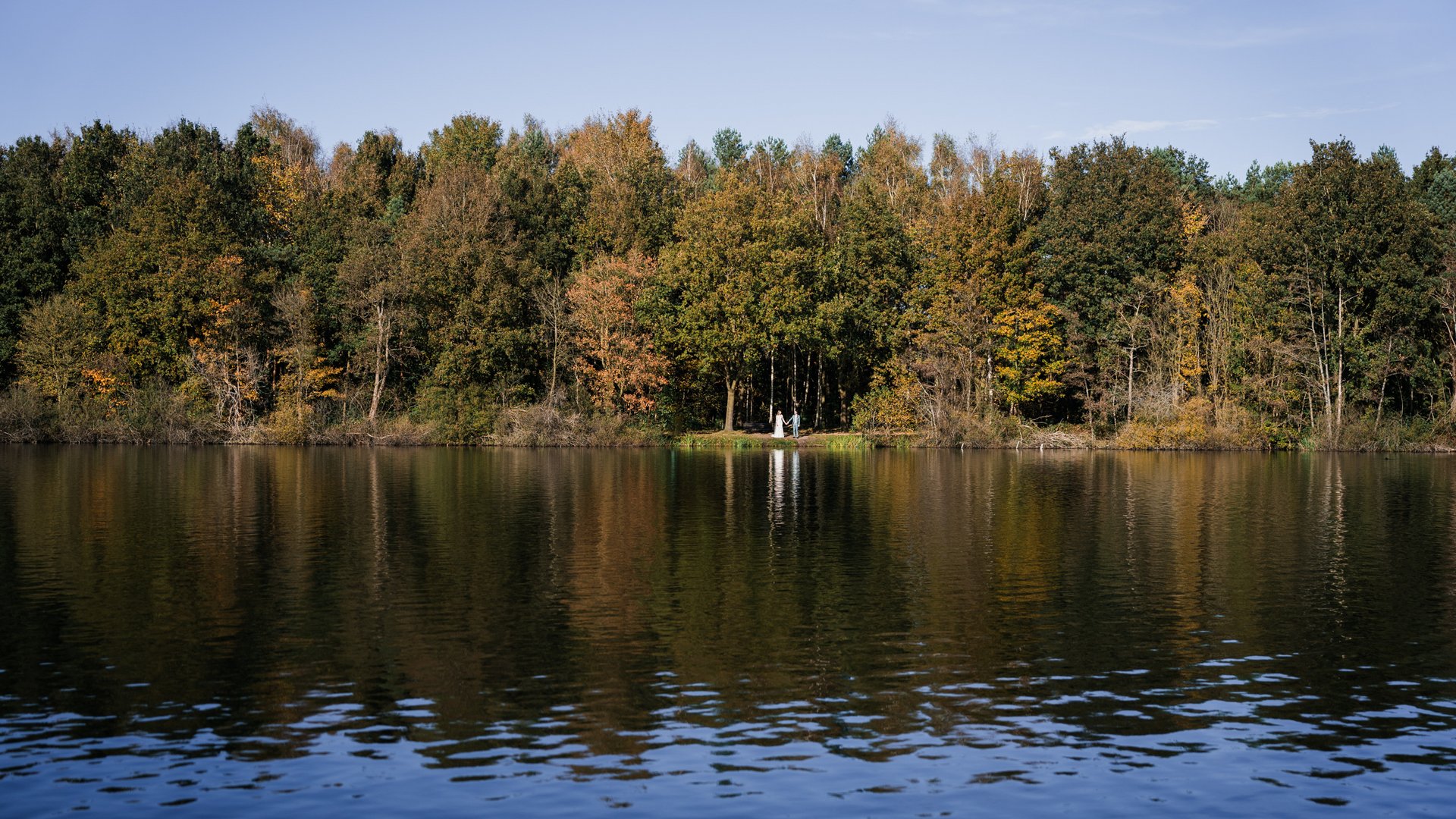 News vom Hotel direkt am See in NRW Ein Paar hält Händchen an einem See vor herbstlichen Bäumen
