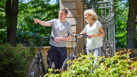 Appartementhotel Seeblick: Bildergalerie Paar mit Fahrrädern, Mann zeigt auf etwas in einem Park