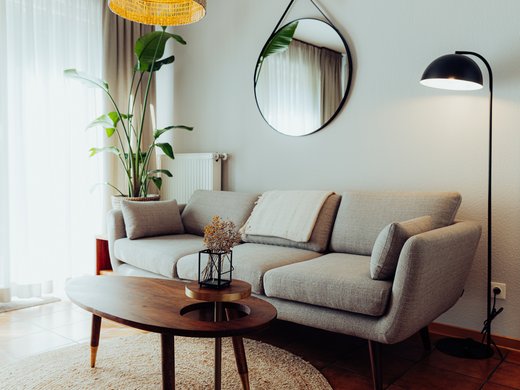 Unsere Appartements am See Gemütliches Wohnzimmer mit grauem Sofa, runder Vase und Stehlampe