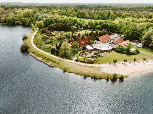 Erholung, Abenteuer und Badespaß für die ganze Familie – direkt am Dreiländersee Luftaufnahme eines Seenufers mit Gebäuden und bewaldetem Hintergrund