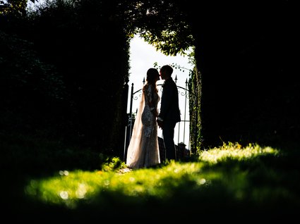 News vom Hotel direkt am See in NRW Braut und Bräutigam stehen sich an einem Gartentor im Gegenlicht gegenüber