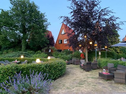 Aparthotel am See in Gronau Garten mit Sitzplätzen und beleuchteten Laternen vor dreieckigen Holzhäusern