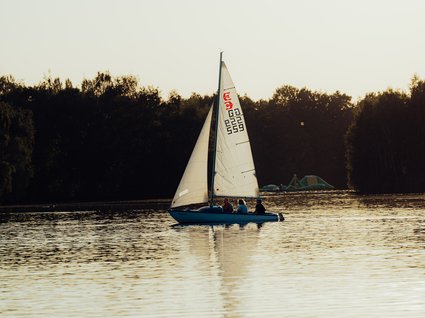 Hotel Seeblick in Gronau Segelboot mit Menschen auf ruhigem See vor bewaldetem Ufer bei Abendlicht