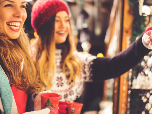 Urlaub am See in NRW - sogar im Winter wunderschön! Zwei lachende Frauen mit Winterkleidung trinken Glühwein auf Weihnachtsmarkt