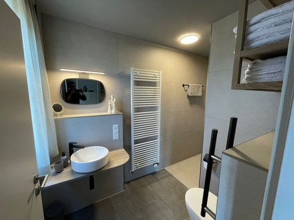 Aparthotel am See in Gronau Modernes Badezimmer mit Waschbecken, Spiegel, Handtuchheizung und Regalen mit Handtüchern