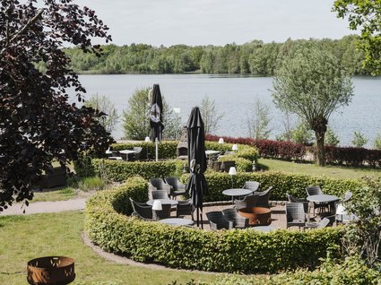 Restaurant Gronau: Seeblick Seating area with tables, chairs, and umbrellas by a lake and trees