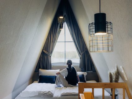 Aparthotel am See in Gronau Person sitzt auf einem Bett in einem gemütlichen Dachzimmer mit Fenster