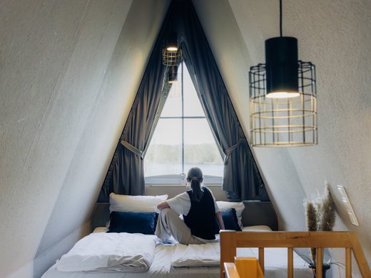 Unsere Appartements am See Persoon zit op een bed in een gezellige zolderkamer met raam