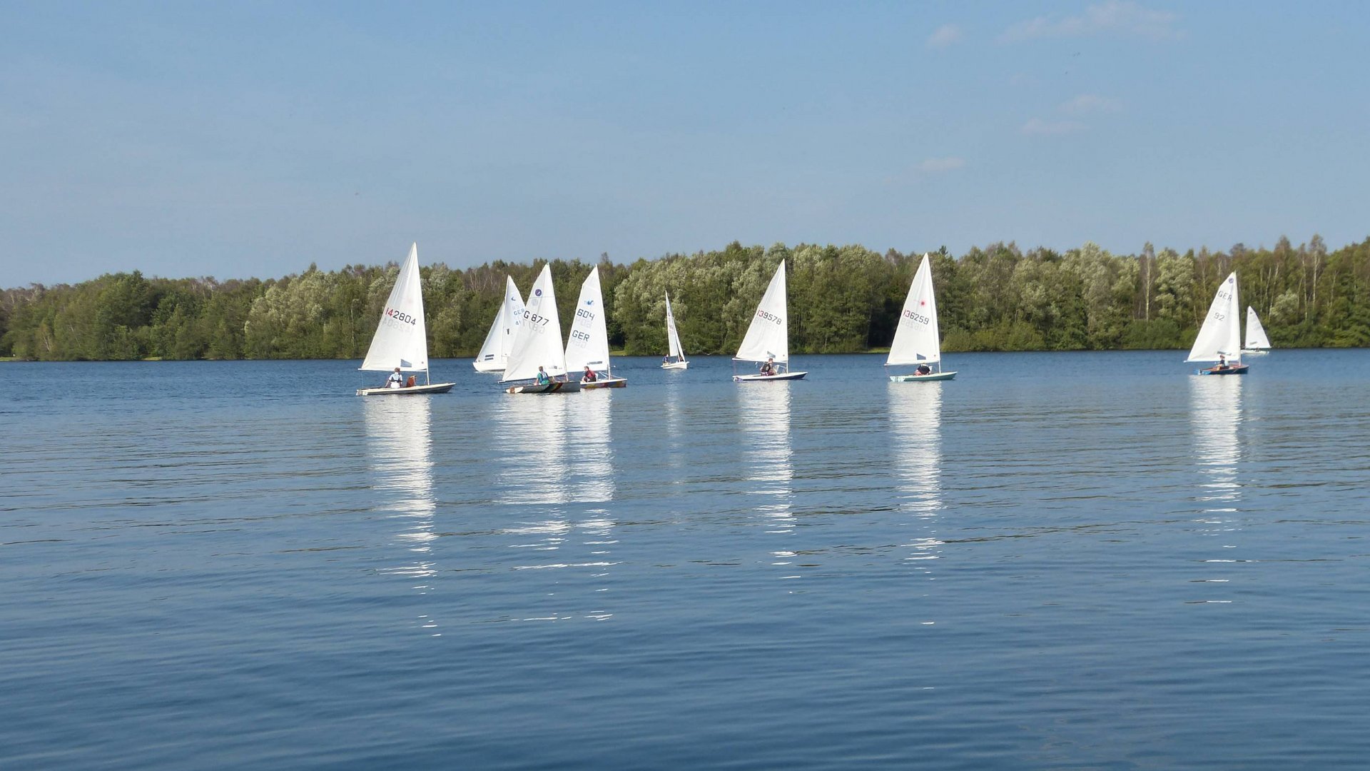 Hotel Seeblick in Gronau Segelboote auf ruhigem See vor bewaldetem Ufer bei klarem Himmel