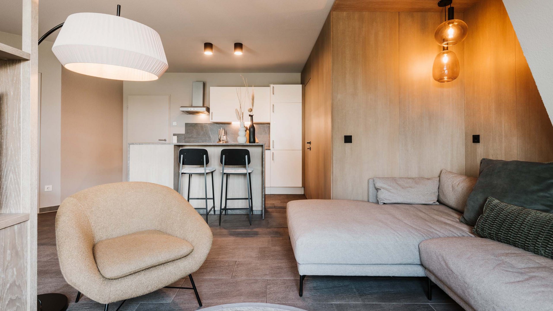 Neuer Look seit März 2023 Modernes Wohnzimmer mit beigem Sessel, grauer Couch und Küche im Hintergrund