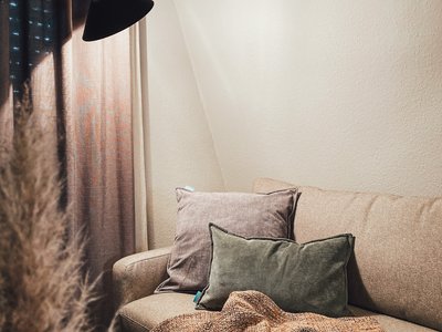 Seeblick: Ferienwohnungen Gronau Gemütliches Sofa mit Kissen, Decke und Lampe in warmem Wohnzimmer