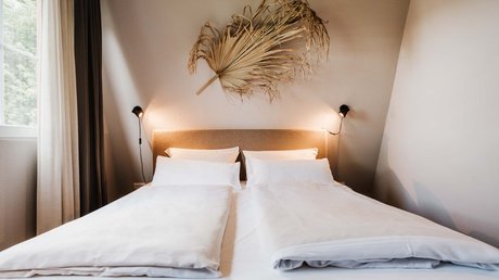 Appartementhotel Seeblick: Bildergalerie Modernes Schlafzimmer mit breitem Doppelbett und dekorativem getrocknetem Palmenblatt an der Wand