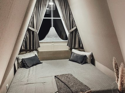 Seeblick: Ferienwohnungen Gronau Gemütliches Bett im spitz zulaufenden Raum mit Vorhängen und Beleuchtung