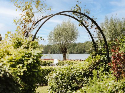 Restaurant Gronau: Seeblick View through a floral arch to a tree by a lake under blue sky
