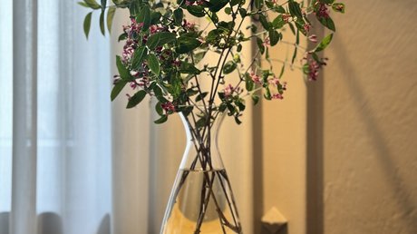 Appartementhotel Seeblick: Bildergalerie Vase mit grünen Zweigen und violetten Blumen auf rundem Holztisch