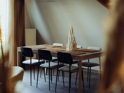 Aparthotel am See in Gronau Essbereich mit Holztisch, sechs Stühlen, Pendelleuchte und Holztreppe
