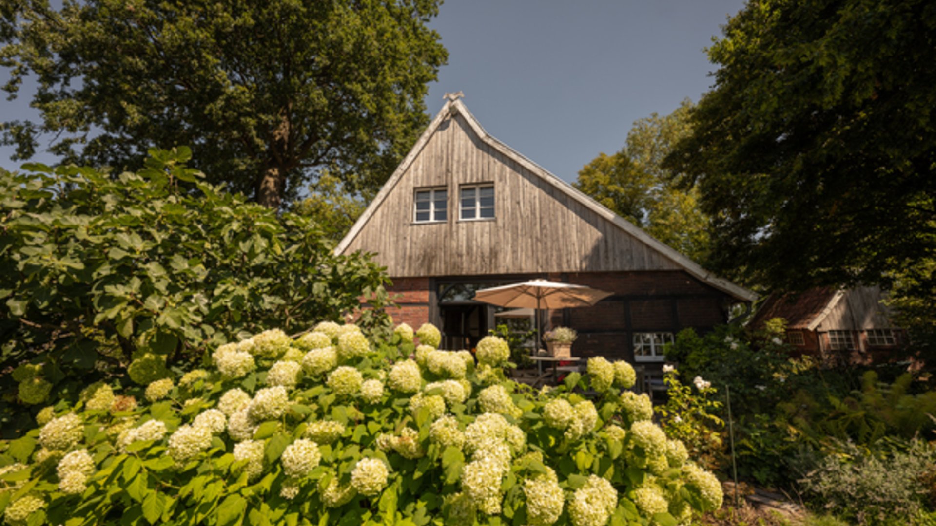 Ihr perfektes Fahrradhotel im Münsterland Traditionelles Haus mit Holzdach und blühendem Garten im Sommer