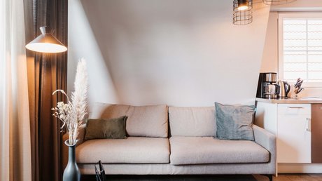 Appartementhotel Seeblick: Bildergalerie Beiges Sofa vor weißer Wand mit Stehlampe und Vase