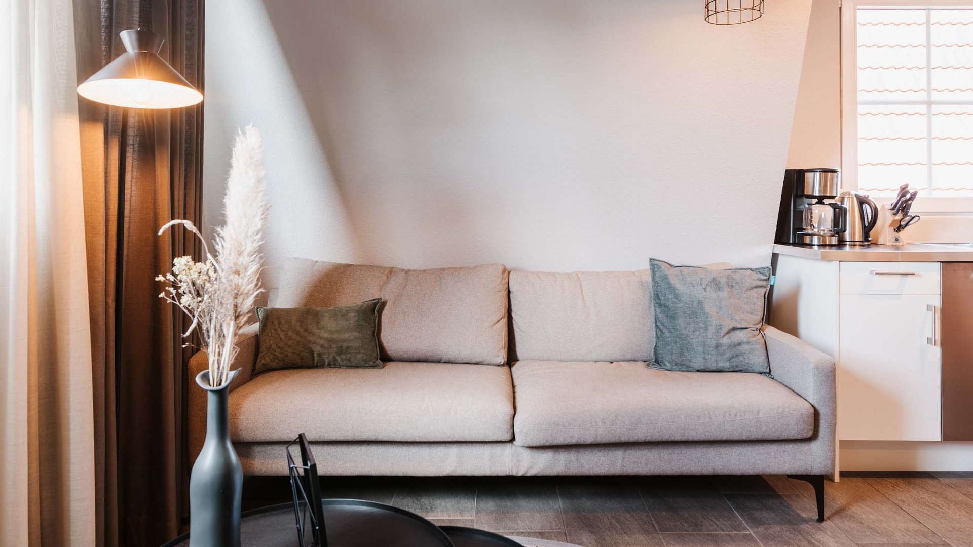 Seeblick: Ferienwohnungen Gronau Beiges Sofa vor weißer Wand mit Stehlampe und Vase