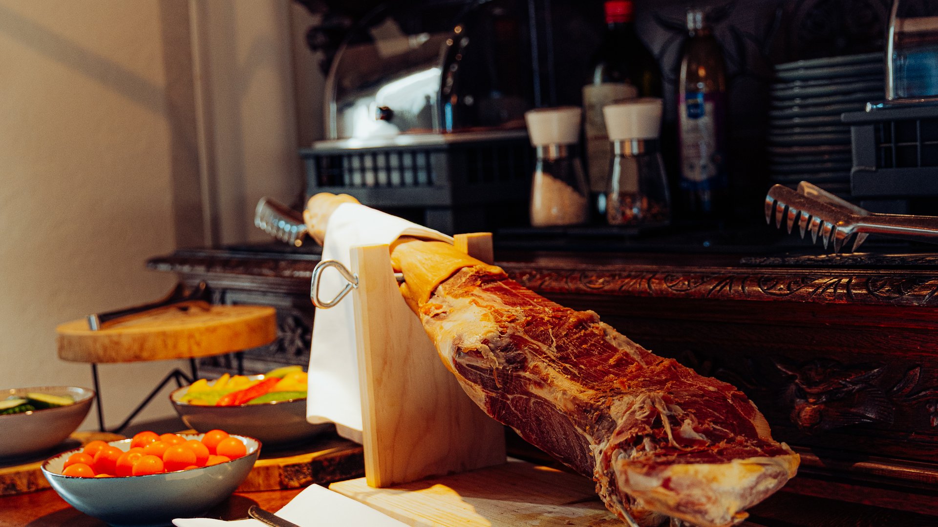 Breakfast at our restaurant Seeblick in Gronau Whole cured ham on a wooden board beside a coffee machine and vegetables