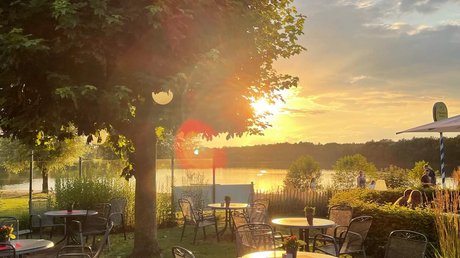 Appartementhotel Seeblick: Bildergalerie Leerer Garten mit Tischen und Stühlen bei Sonnenuntergang am See