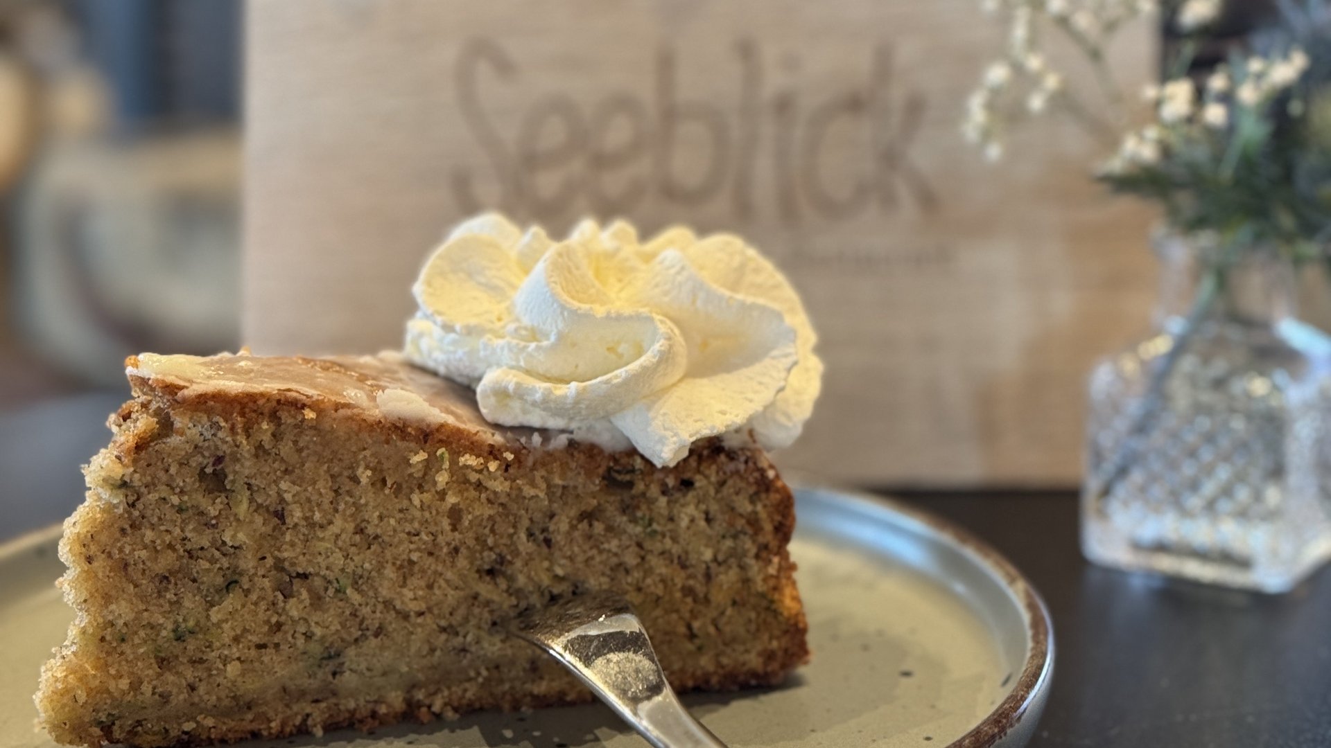 Restaurant Seeblick: Speisekarte Ein Stück Kuchen mit Sahne auf einem Teller mit Blick auf ein Holzschild mit Schrift