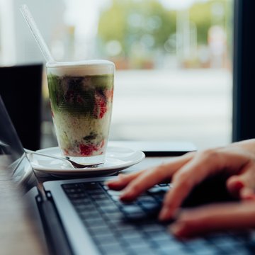 Jobs im Hotel Restaurant Seeblick in Gronau Hände tippen auf einem Laptop neben einem geschichteten Getränk im Glas mit Strohhalm