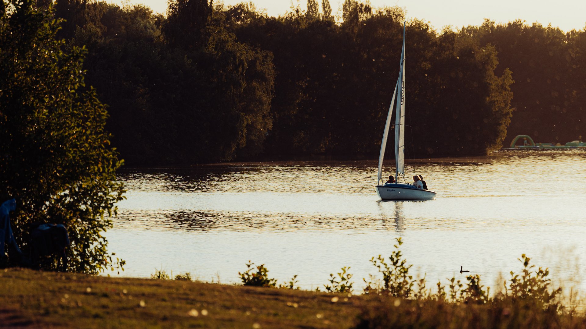 Jobs im Hotel Restaurant Seeblick in Gronau Segelboot auf ruhigem See bei Sonnenuntergang mit bewaldetem Ufer