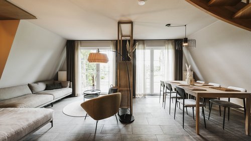 Hotel Seeblick in Gronau Modernes Wohnzimmer mit Sofa, Sessel, großem Esstisch und großen Fenstern
