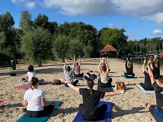 Strand Yoga am Dreiländersee in Gronau Menschen machen Yoga auf Yogamatten am Sandstrand bei bewölktem Himmel