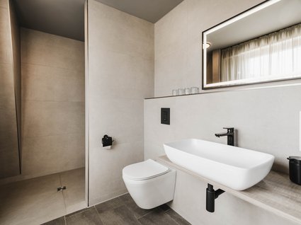 Holidays in an apartment with a lake view Modern bathroom with wall-mounted toilet, sink, and illuminated mirror