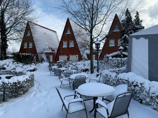 Hiking in North Rhine-Westphalia at any time of year Snow-covered tables and chairs in front of three pointed wooden houses in winter