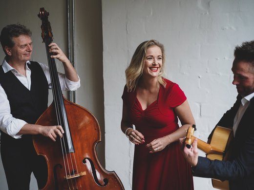Seeblick Gronau: Urlaub inmitten der Natur Drei Musiker gemeinsam mit Kontrabass, Gitarre und Sängerin in rotem Kleid