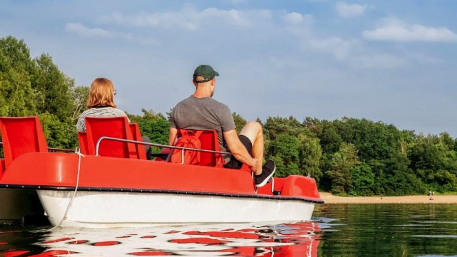 Erholung, Abenteuer und Badespaß für die ganze Familie – direkt am Dreiländersee Zwei Personen auf einem roten Tretboot auf einem ruhigen See