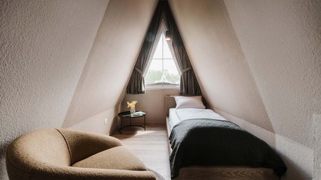 Appartementhotel Seeblick: Bildergalerie Kleines gemütliches Schlafzimmer unter einem spitzen Dach mit einem Bett und Sessel