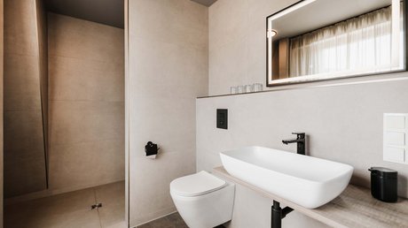Appartementhotel Seeblick: Bildergalerie Modernes Badezimmer mit Wandtoilette, Waschbecken und beleuchtetem Spiegel