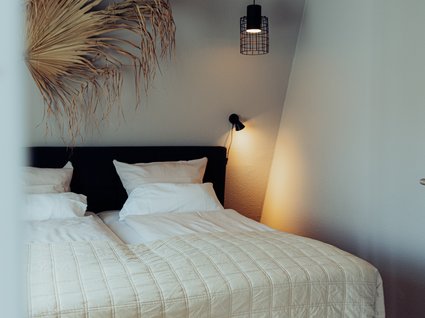 Aparthotel am See in Gronau Schlafzimmer mit Doppelbett, weißer Bettwäsche und schwarzen Hängeleuchten