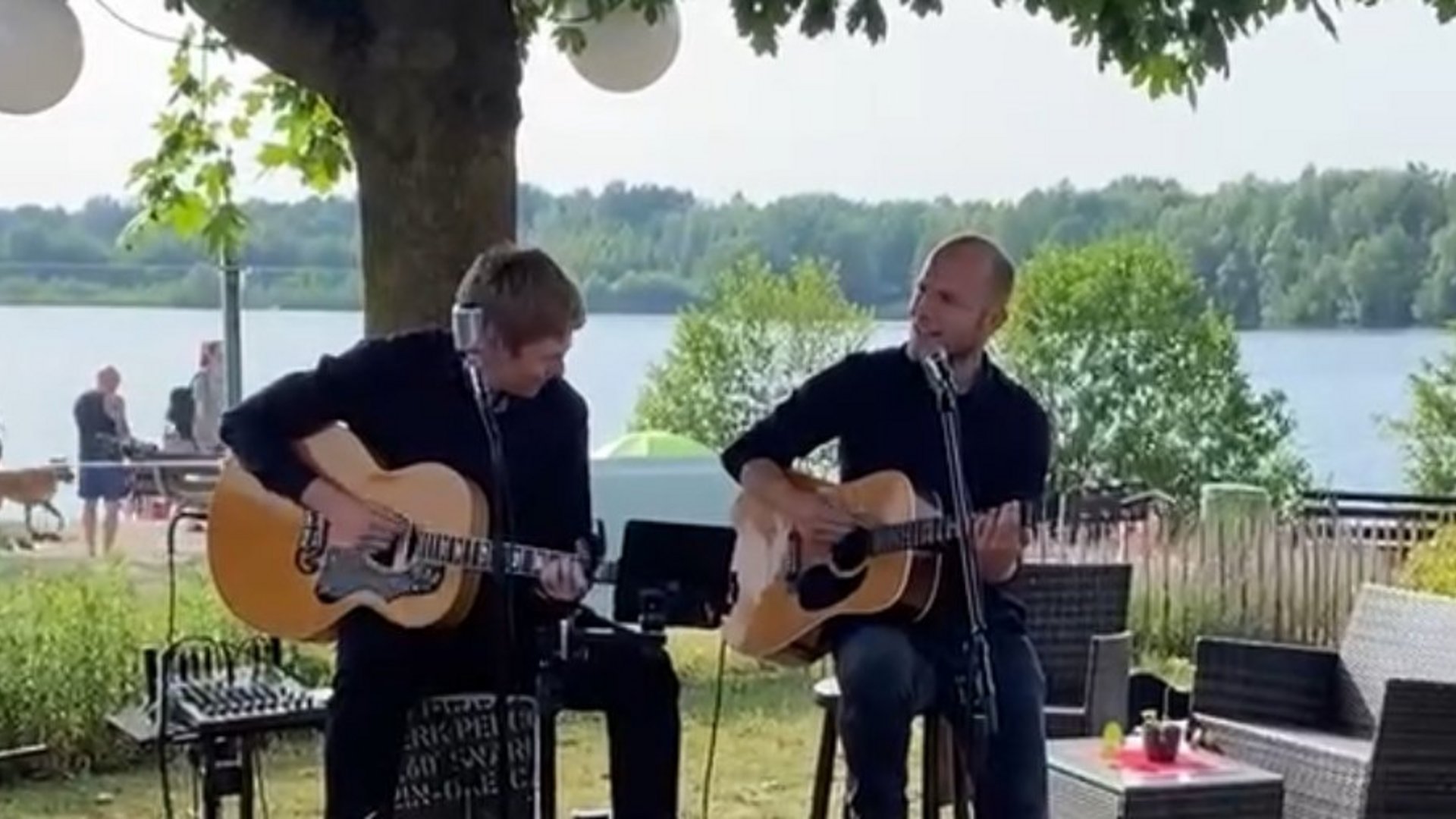 Live-Musik Event im Münsterland am See Zwei Musiker spielen Akustikgitarre unter einem Baum am See