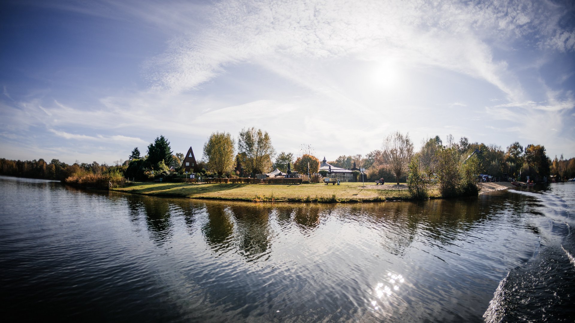 Insel mit Bäumen und Häusern am ruhigen See unter bewölktem Himmel