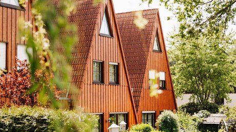 Appartementhotel Seeblick: Bildergalerie Holzhaus mit spitzem Dach und grüner Gartenanlage im Sonnenschein