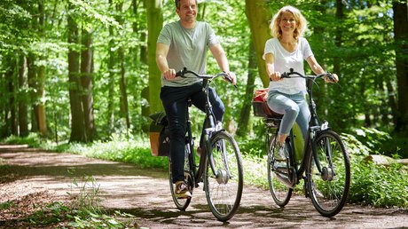 Appartementhotel Seeblick: Bildergalerie Glückliches Paar fährt Fahrrad auf Waldweg bei Sonnenschein