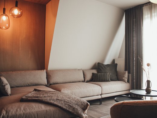 Onze appartementen aan het meer Gezellige woonkamer met grijze bank, salontafel en warme hanglampen