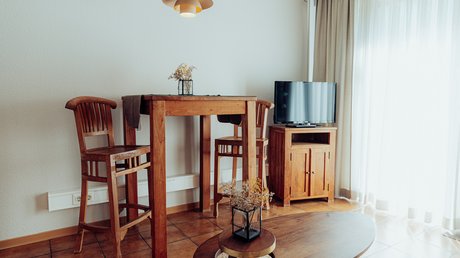 Appartementhotel Seeblick: Bildergalerie Kleiner Wohnbereich mit Holzhochstuhl, Tisch und TV auf Holzkommode