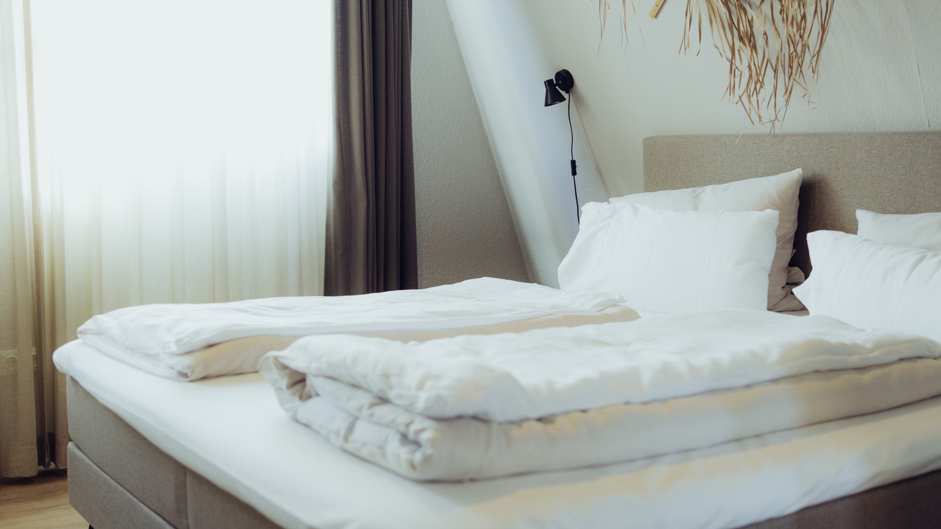 Hotel Seeblick in Gronau Modernes Schlafzimmer mit Doppelbett, weißen Bettdecken und getrockneter Wanddekoration