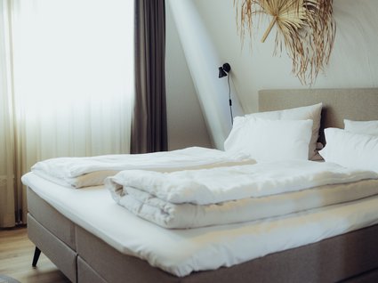 Aparthotel am See in Gronau Modernes Schlafzimmer mit Doppelbett, weißen Bettdecken und getrockneter Wanddekoration