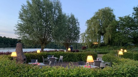 Appartementhotel Seeblick: Bildergalerie Abendliche Terrasse mit beleuchteten Tischen neben einem See und Bäumen
