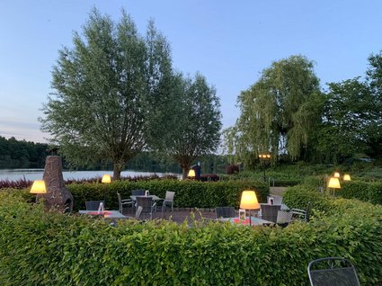 Holidays in an apartment with a lake view Evening terrace with lit tables beside a lake and trees